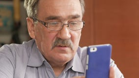 An elderly man with a mustache in glasses dials a text message on his mobile phone. Sits at home at the table. stock video An elderly man with a mustache in glasses dials a text message on his mobile phone. Sits at home at the table. stock video