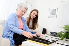 Elderly woman with her young granddaughter at home looking at memory in family photo album Stock Photo Elderly woman with her young granddaughter at home looking at memory in family photo album Stock Photo