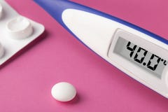 Electronic thermometer and pills on a pink background. High temperature 40 degrees Celsius on display stock photo Electronic thermometer and pills on a pink background. High temperature 40 degrees Celsius on display stock photo