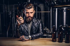 Elegancki brodaty rowerzysta ubierał czarnego skórzanej kurtki obsiadanie przy barem odpierającym w indie browarze obrazy royalty free Elegancki brodaty rowerzysta ubierał czarnego skórzanej kurtki obsiadanie przy barem odpierającym w indie browarze obrazy royalty free