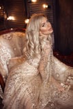 Elegant blond kvinna i den beigea klänningen som poserar på den lyxiga soffan i kunglig inre Härlig sinnlig brud för mode med mak royaltyfria foton Elegant blond kvinna i den beigea klänningen som poserar på den lyxiga soffan i kunglig inre Härlig sinnlig brud för mode med mak royaltyfria foton