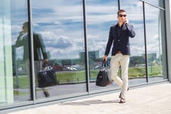 Elegant businessman call on mobile phone while walking with suitcase outside airport Stock Photography Elegant businessman call on mobile phone while walking with suitcase outside airport Stock Photography