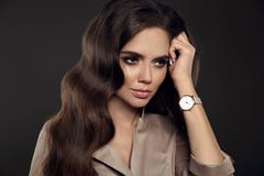 Elegant lady with Watch on hand. Beautiful woman with long healthy wavy hair style posing in studio on dark background stock photo Elegant lady with Watch on hand. Beautiful woman with long healthy wavy hair style posing in studio on dark background stock photo