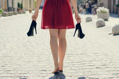 Elegant Young Girl In Red Dress With High-heels In Hands, Walking On The Street Barefoot. She Is Coming Back Home After Party In Royalty Free Stock Photos