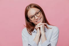 Elegante hübsche Frau kippt Kopf, hält Hände unter Kinn, trägt transparente Gläser und Hemd, lächelt leicht, Modelle über Rosa stockfoto Elegante hübsche Frau kippt Kopf, hält Hände unter Kinn, trägt transparente Gläser und Hemd, lächelt leicht, Modelle über Rosa stockfoto