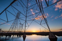 Elektrische Türme mit Leitlinien bei Sonnenuntergang, mit Reflexionen im Wasser stockbild Elektrische Türme mit Leitlinien bei Sonnenuntergang, mit Reflexionen im Wasser stockbild