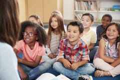 Elementary school kids sit on floor looking up at teacher stock photography Elementary school kids sit on floor looking up at teacher stock photography