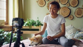 Emotional girl successful blogger is recording video for her online vlog sitting on bed in modern apartment and stroking stock video footage Emotional girl successful blogger is recording video for her online vlog sitting on bed in modern apartment and stroking stock video footage