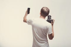 Emotionele Mens met camera die op lichte achtergrond wordt geïsoleerd De digitale camera en smartphone van de jonge mensengreep L stock foto Emotionele Mens met camera die op lichte achtergrond wordt geïsoleerd De digitale camera en smartphone van de jonge mensengreep L stock foto