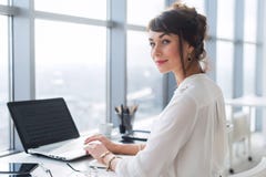 Empleado de oficina de sexo femenino joven que usa el ordenador portátil en el trabajo, sonrisa, mirando la cámara Empresaria que fotos de archivo libres de regalías Empleado de oficina de sexo femenino joven que usa el ordenador portátil en el trabajo, sonrisa, mirando la cámara Empresaria que fotos de archivo libres de regalías