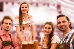 A empregada de mesa entrega cervejas na barraca com visitantes felizes em uma barraca da cerveja em Munich Oktoberfest imagem de stock royalty free A empregada de mesa entrega cervejas na barraca com visitantes felizes em uma barraca da cerveja em Munich Oktoberfest imagem de stock royalty free