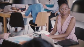 Empresaria femenina afroamericana con el smartphone que se sienta por la tabla de la oficina en la cámara lenta coworking moderna almacen de metraje de vídeo Empresaria femenina afroamericana con el smartphone que se sienta por la tabla de la oficina en la cámara lenta coworking moderna almacen de metraje de vídeo