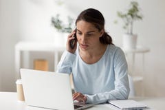 Empresaria seria que habla por el tel?fono que trabaja en el ordenador port?til imagenes de archivo Empresaria seria que habla por el tel?fono que trabaja en el ordenador port?til imagenes de archivo