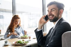 Empresários que têm o almoço de negócio no homem de assento do restaurante que fala no close-up do smartphone quando mulher que c imagens de stock Empresários que têm o almoço de negócio no homem de assento do restaurante que fala no close-up do smartphone quando mulher que c imagens de stock