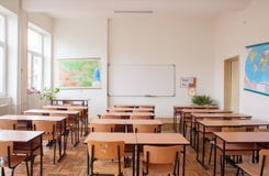 Empty classroom. Interior with wooden desks and chairs, maps and white board Empty classroom. Interior with wooden desks and chairs, maps and white board