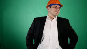 En attraktiv man i en orange konstruktionshjälm och dräkt ser kameran En ung arbetare visar gester med hans arkivfilmer En attraktiv man i en orange konstruktionshjälm och dräkt ser kameran En ung arbetare visar gester med hans arkivfilmer