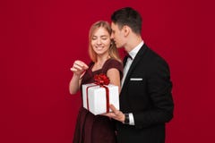 En elegant man i en dräkt ger en överraskning till en kvinna, ger henne en gåva, på en röd bakgrund, begreppet av kvinnors dag arkivfoto En elegant man i en dräkt ger en överraskning till en kvinna, ger henne en gåva, på en röd bakgrund, begreppet av kvinnors dag arkivfoto