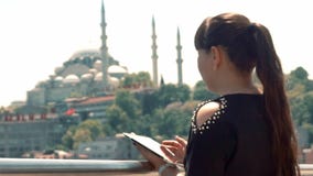 En flicka av asiatiska utseendemässiga ställningar nära en härlig sikt av staden och blickar på hennes minnestavla arkivfilmer En flicka av asiatiska utseendemässiga ställningar nära en härlig sikt av staden och blickar på hennes minnestavla arkivfilmer