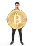 En gladlynt man på en vit bakgrund som rymmer ett enormt bitcoinmynt royaltyfria bilder En gladlynt man på en vit bakgrund som rymmer ett enormt bitcoinmynt royaltyfria bilder