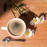 En kopp av svart kaffe, försilvrar skeden, filial av blommor för den vita tusenskönan på bästa sikt för träbakgrund royaltyfri foto En kopp av svart kaffe, försilvrar skeden, filial av blommor för den vita tusenskönan på bästa sikt för träbakgrund royaltyfri foto