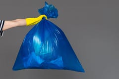 En kvinnas hand i en gummihandske rymmer en blå plastpåse mycket av avskräde arkivbilder En kvinnas hand i en gummihandske rymmer en blå plastpåse mycket av avskräde arkivbilder