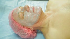En kvinnlig cosmetologist som bär handskar, applicerar en havsväxtmaskering till en framsida för man s med en borste lager videofilmer En kvinnlig cosmetologist som bär handskar, applicerar en havsväxtmaskering till en framsida för man s med en borste lager videofilmer