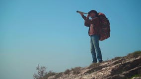 En man i en cowboyhatt, piskar omslaget, jeans, en turist- ryggs?ck p? hans skuldror En man ser till och med ett teleskop arkivfilmer En man i en cowboyhatt, piskar omslaget, jeans, en turist- ryggs?ck p? hans skuldror En man ser till och med ett teleskop arkivfilmer
