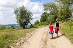 En pojke och barn för en flicka går på en grusväg på en solig sommardag Ungar som tillsammans rymmer händer, medan tycka om ativi royaltyfria foton En pojke och barn för en flicka går på en grusväg på en solig sommardag Ungar som tillsammans rymmer händer, medan tycka om ativi royaltyfria foton
