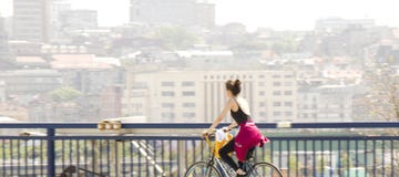 En ridningcykel för ung kvinna på stadsgatabron med oskarp ljus cityscapebakgrund royaltyfria bilder En ridningcykel för ung kvinna på stadsgatabron med oskarp ljus cityscapebakgrund royaltyfria bilder