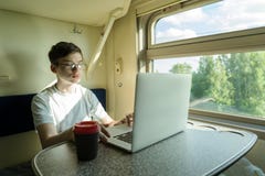 En tonåringpojke på ett drev sitter på en tabell med en öppen dator royaltyfri fotografi En tonåringpojke på ett drev sitter på en tabell med en öppen dator royaltyfri fotografi