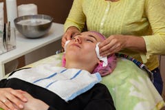 En ung flicka ligger p? en soffa under kosmetiska tillv?gag?ngss?tt med en maskering p? framsidan som kosmetologkvinnan pressar o royaltyfri fotografi En ung flicka ligger p? en soffa under kosmetiska tillv?gag?ngss?tt med en maskering p? framsidan som kosmetologkvinnan pressar o royaltyfri fotografi