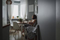 En ung kvinna med ett behandla som ett barnsammanträde i ett hemtrevligt grått kök och blickar ut fönstret royaltyfri bild En ung kvinna med ett behandla som ett barnsammanträde i ett hemtrevligt grått kök och blickar ut fönstret royaltyfri bild