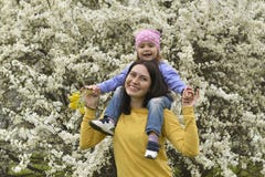 En ung moder har satt hennes lilla dotter pÃ¥ hennes skuldror och lekar med henne i den blommande trädgÃ¥rden fotografering för bildbyråer En ung moder har satt hennes lilla dotter pÃ¥ hennes skuldror och lekar med henne i den blommande trädgÃ¥rden fotografering för bildbyråer