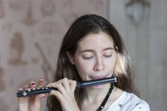 En ursnygg ung kvinna som sitter och spelar flöjtpickolaflöjten royaltyfri fotografi En ursnygg ung kvinna som sitter och spelar flöjtpickolaflöjten royaltyfri fotografi