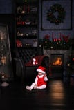 Enfant assez petit dans le chapeau de Santa près de l'arbre de Cristmas le bébé s'assied sur seul le plancher près de la cheminée photo libre de droits Enfant assez petit dans le chapeau de Santa près de l'arbre de Cristmas le bébé s'assied sur seul le plancher près de la cheminée photo libre de droits