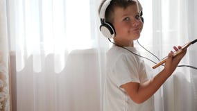 Enfant de sourire avec le téléphone dans des mains écoutant la musique à travers le casque et dansant dans la chambre clips vidéos Enfant de sourire avec le téléphone dans des mains écoutant la musique à travers le casque et dansant dans la chambre clips vidéos