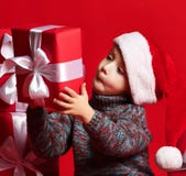 Enfant drôle de sourire dans le chapeau rouge de Santa jugeant le cadeau de Noël disponible Concept de Noël photo stock Enfant drôle de sourire dans le chapeau rouge de Santa jugeant le cadeau de Noël disponible Concept de Noël photo stock