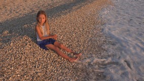 Enfant jouant sur la plage, enfant au coucher du soleil, cailloux de lancement de fille en eau de mer photographie stock libre de droits Enfant jouant sur la plage, enfant au coucher du soleil, cailloux de lancement de fille en eau de mer photographie stock libre de droits