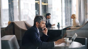 Entreprenör, i samtal på mobiltelefonen och att använda bärbar datorarbete i kafé lager videofilmer Entreprenör, i samtal på mobiltelefonen och att använda bärbar datorarbete i kafé lager videofilmer