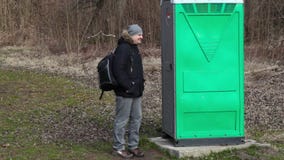 Equipaggi l'attesa vicino alla toilette portatile verde nel parco Equipaggi l'attesa vicino alla toilette portatile verde nel parco