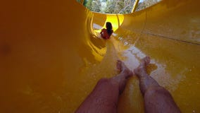 Equipaggi scendere l'acquascivolo colorato e prende ragazza nella parte anteriore con spruzzata dell'acqua nel parco dell'acqua s Equipaggi scendere l'acquascivolo colorato e prende ragazza nella parte anteriore con spruzzata dell'acqua nel parco dell'acqua s