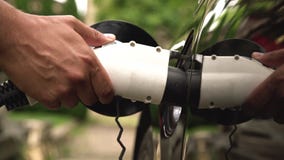 Equipaggia la mano che inserisce la spina del caricatore nell'automobile elettrica nel fondo verde dell'ambiente Il nuovo veicolo stock footage Equipaggia la mano che inserisce la spina del caricatore nell'automobile elettrica nel fondo verde dell'ambiente Il nuovo veicolo stock footage