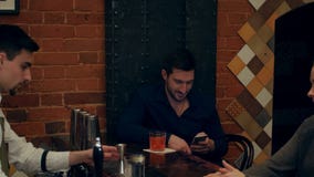 Equipe usando um smartphone e olhando fixamente na mulher bonita nova atrás dele, quando empregado de bar que prepara um cocktail video estoque Equipe usando um smartphone e olhando fixamente na mulher bonita nova atrás dele, quando empregado de bar que prepara um cocktail video estoque