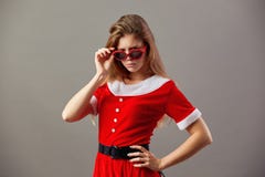 Ernstige charmante Mevr. Santa Claus in zonnebril kleedde zich in de rode robe en de witte handschoenentribunes op de grijze acht stock afbeelding Ernstige charmante Mevr. Santa Claus in zonnebril kleedde zich in de rode robe en de witte handschoenentribunes op de grijze acht stock afbeelding