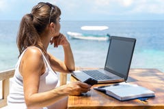 Escritor bonito joven del freelancer de la mujer que trabaja con la libreta del ordenador portátil y el teléfono delante del mar Imágenes de archivo libres de regalías Escritor bonito joven del freelancer de la mujer que trabaja con la libreta del ordenador portátil y el teléfono delante del mar Imágenes de archivo libres de regalías