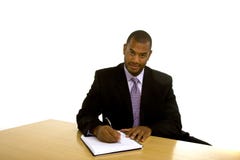 Escritura del hombre negro en el escritorio que mira la cámara imagen de archivo Escritura del hombre negro en el escritorio que mira la cámara imagen de archivo