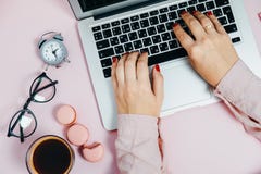 Escritura femenina de la mano de la endecha plana en el ordenador portátil en los macarrones rosados a de la planta foto de archivo libre de regalías Escritura femenina de la mano de la endecha plana en el ordenador portátil en los macarrones rosados a de la planta foto de archivo libre de regalías