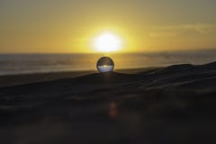 Esfera de cristal empoleirada na areia em um por do sol imagem de stock royalty free Esfera de cristal empoleirada na areia em um por do sol imagem de stock royalty free