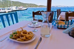 Essen des gebratenen Kalmars und Trinken des Weißweins in einem Schatten eines typischen griechischen taverna lizenzfreie stockfotografie Essen des gebratenen Kalmars und Trinken des Weißweins in einem Schatten eines typischen griechischen taverna lizenzfreie stockfotografie
