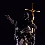 Estatua de un santo del puente que lleva a cabo una cruz de oro grande en la noche fotografía de archivo libre de regalías Estatua de un santo del puente que lleva a cabo una cruz de oro grande en la noche fotografía de archivo libre de regalías